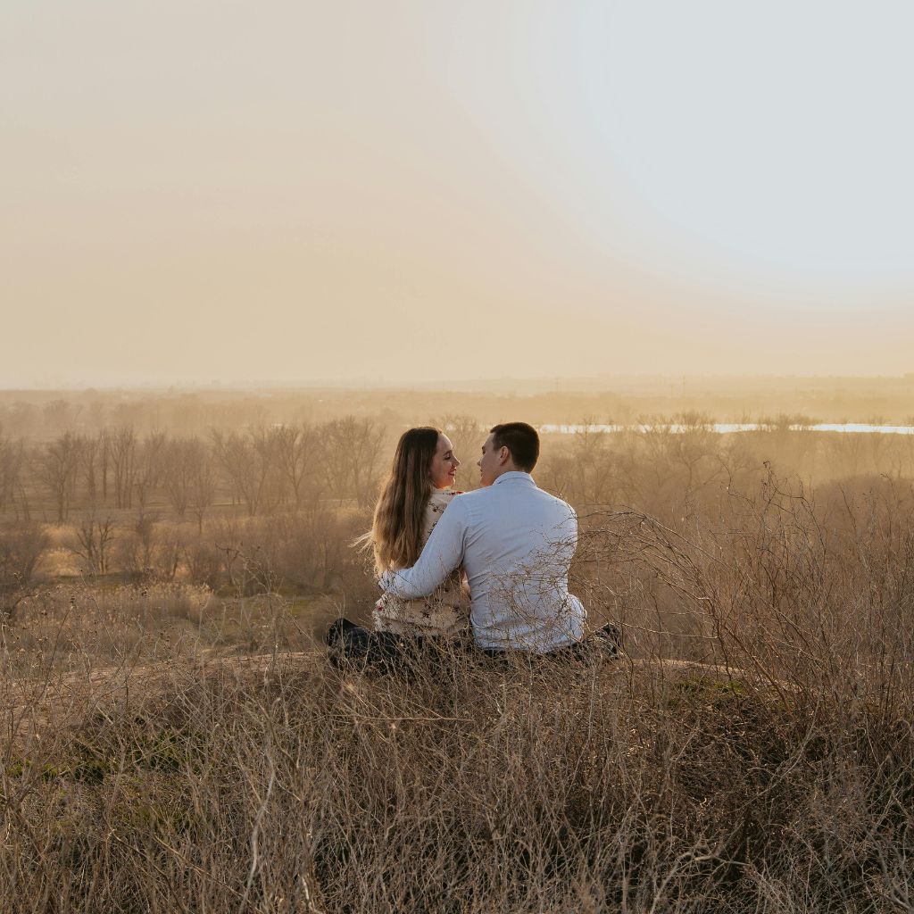 Couple sitting together in a field overlooking a peaceful natural landscape