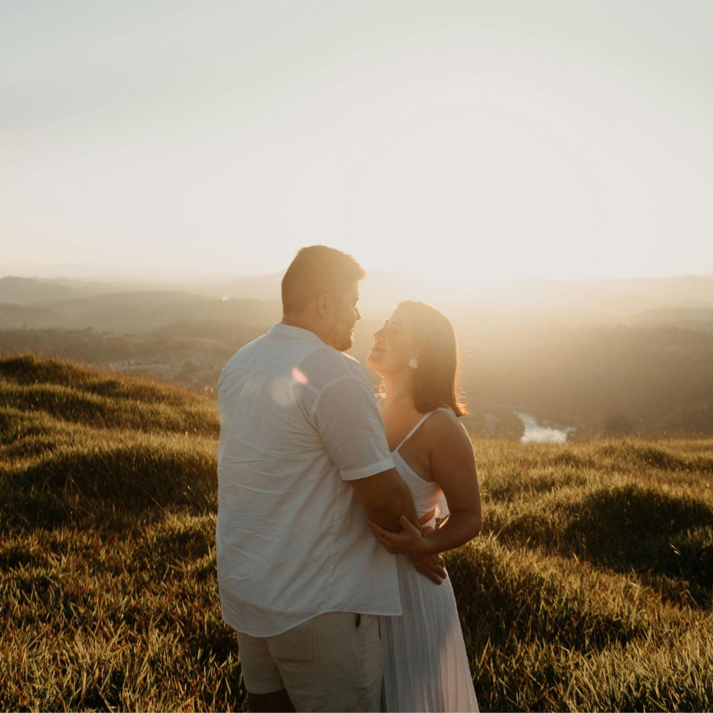Couple embracing and watching the sunset together in a grassy field