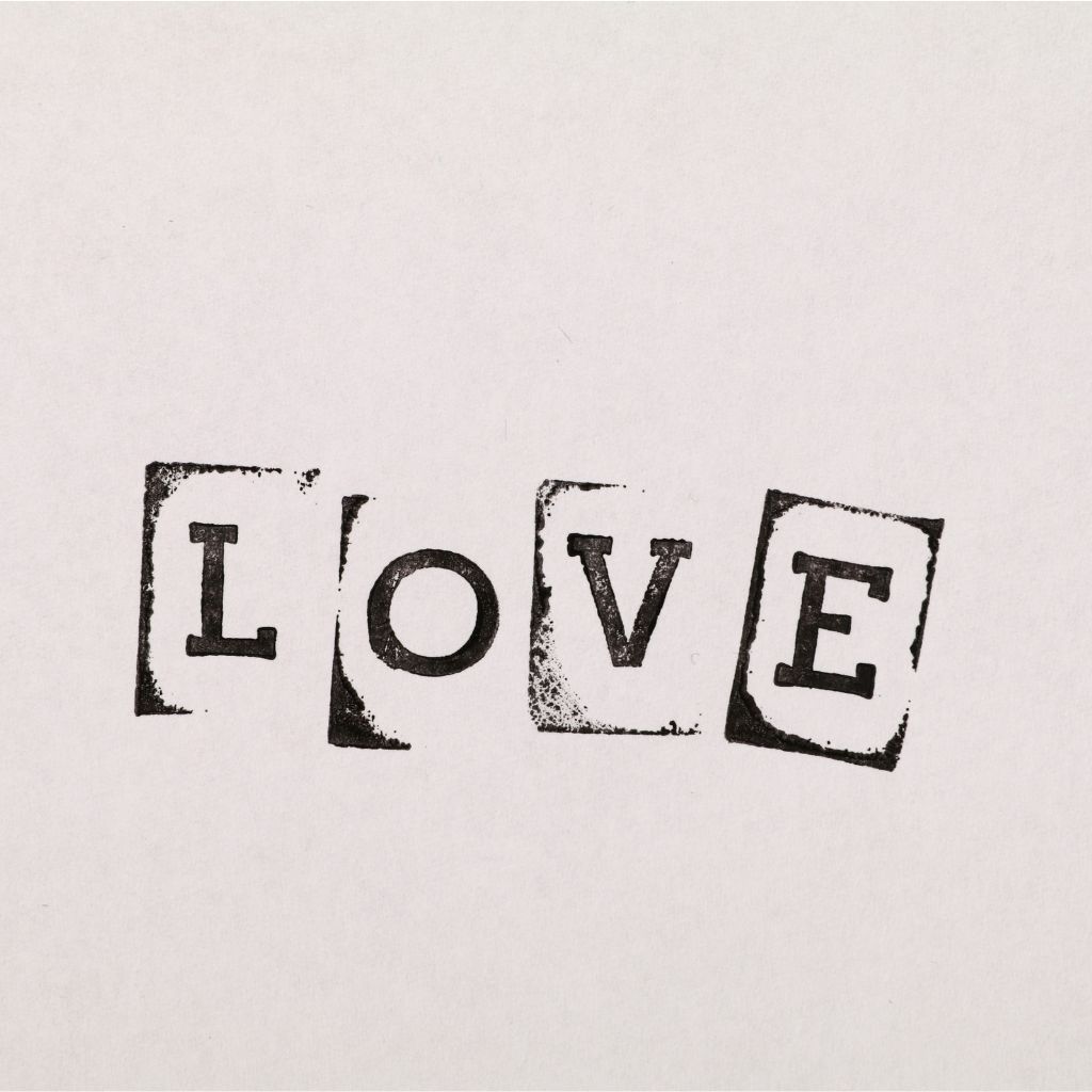 The word “LOVE” is displayed in bold black stamped letters on separate slightly tilted square pieces of paper.