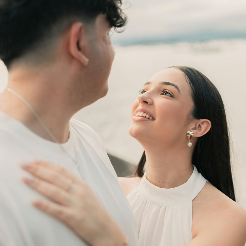 Young couple looking lovingly at each other outdoors, with the woman smiling brightly.