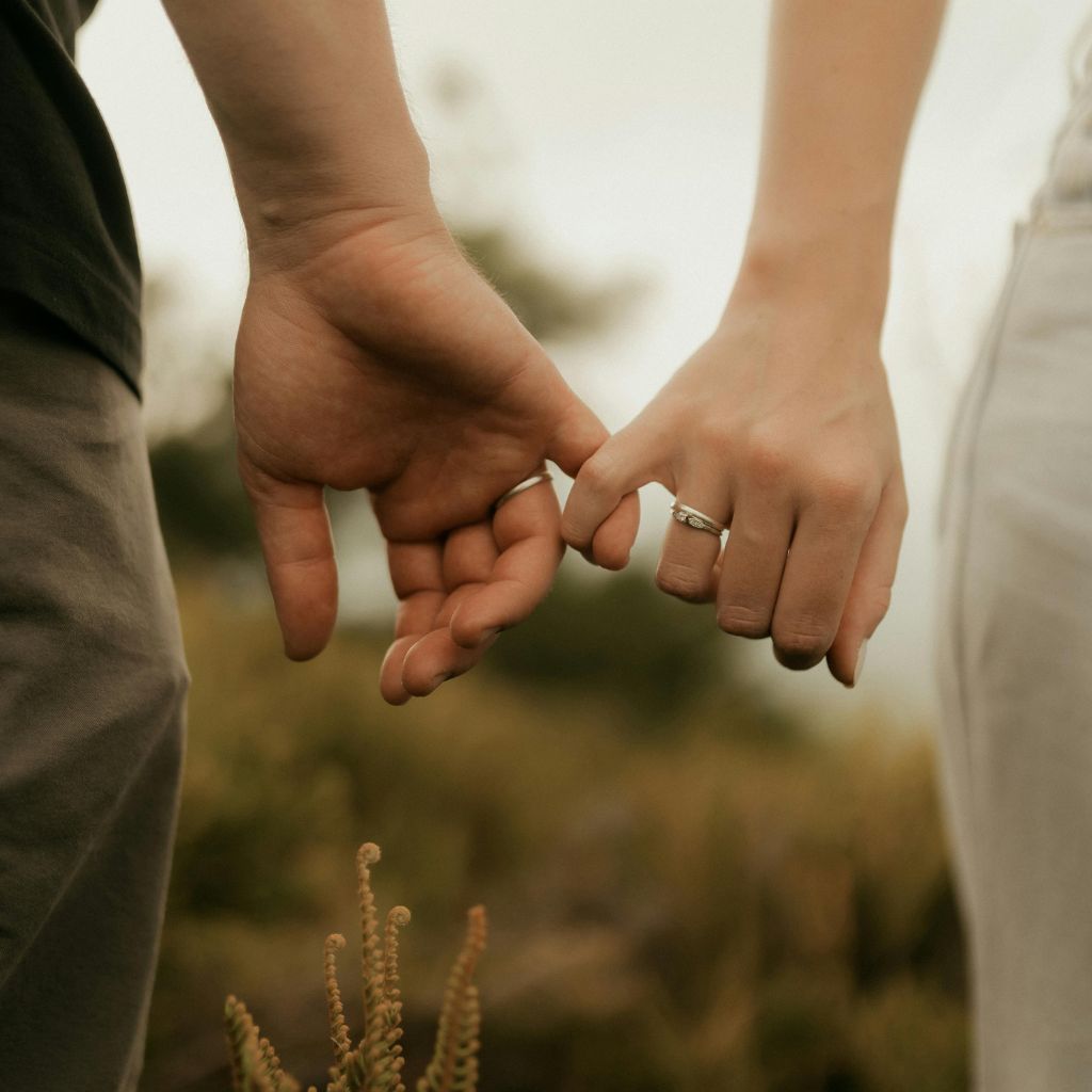 Close-up of a couple gently linking fingers while walking outdoors, with rings visible on their hands.