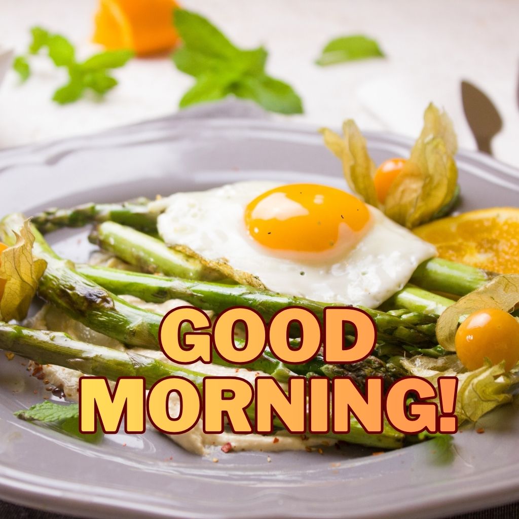 A sunny-side-up egg over roasted asparagus on a gray plate with bold text reading "GOOD MORNING!" across the image.