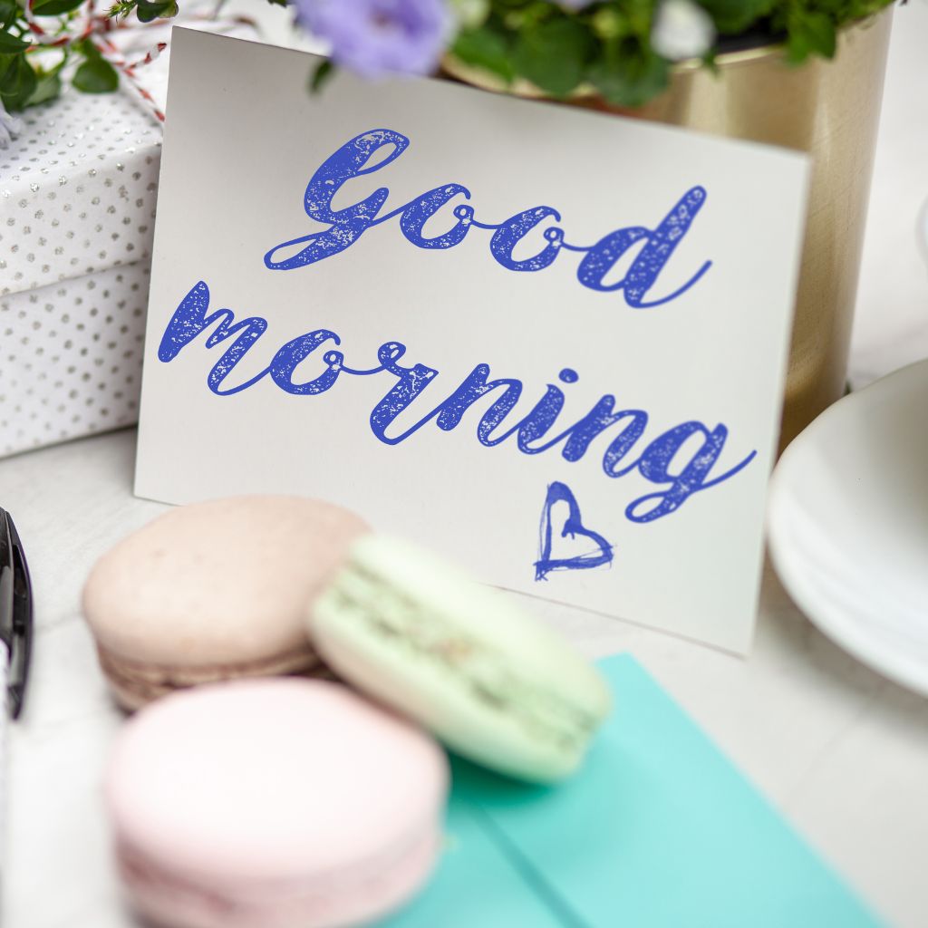 A cheerful good morning card featuring colorful macarons and vibrant flowers, conveying a warm greeting.